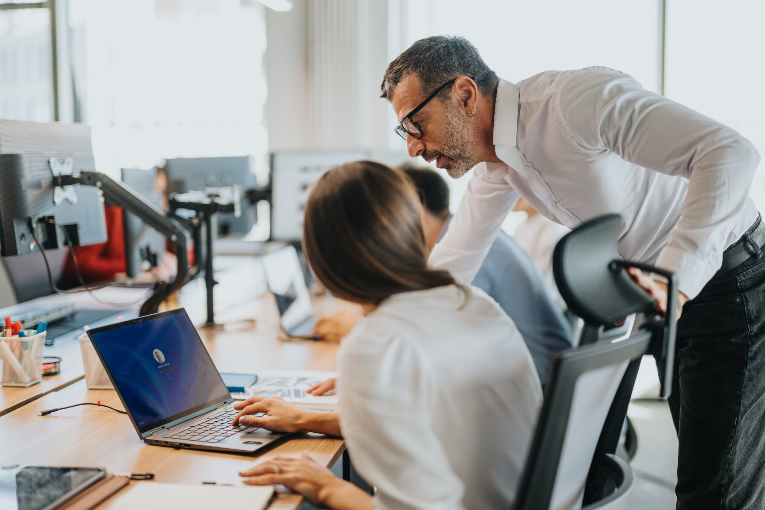 Business people working together in an open office space, focusing on teamwork and collaboration. IT support assists employees